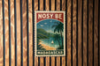 A vintage-style postage stamp from Madagascar, featuring a tropical beach scene with palm trees and a sailboat, is displayed on a wooden wall.