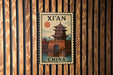 A vintage-style postage stamp featuring a traditional Chinese temple, mounted on a wooden wall.