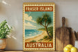 A framed vintage-style stamp depicting a tropical beach scene with palm trees and the ocean, placed on a shelf next to a wooden cutting board and some lemons.