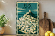 A framed poster of a Greek village with a mountain in the background, displayed on a wall next to a wooden cutting board and some potted plants.