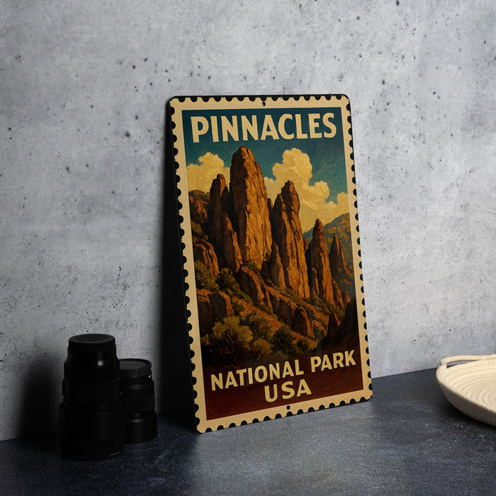A vintage-style metal sign for Pinnacles National Park, featuring a mountain landscape with a cloudy sky.