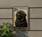A black and white postage stamp featuring a dog's portrait, mounted on a wall next to a plant.