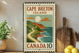 A vintage-style metal sign for Cape Breton Island, Canada, featuring a scenic illustration of a winding road leading to a mountainous coastline with a bright sun and clouds.