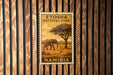 a stamp or postcard with an illustration of an elephant and the text "ETOSHA NATIONAL PARK NAMIBIA" on it, which is mounted on a wooden wall.