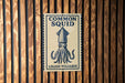 a sign with the text "Common Squid" and "Loligo Vulzaris" on it, which is mounted on a wooden wall.