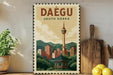 A vintage-style poster of the Daegu Tower, a famous landmark in South Korea, displayed on a wall next to a wooden cutting board and some potted plants.