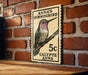 A wooden table with a framed image of a hummingbird, which appears to be a postage stamp or a decorative piece.
