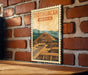 A framed illustration of the Teotihuacan pyramid in Mexico is displayed on a brick wall.