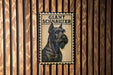 A framed poster of a giant schnauzer dog is displayed on a wooden wall.