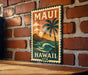 A vintage-style metal sign with the text "MAUI HAWAII USA" and a palm tree illustration is displayed on a brick wall.
