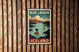 A vintage-style poster of the Blue Lagoon in Iceland, featuring a woman in a bathing suit and a scenic landscape with mountains and water.