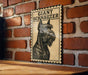 A framed poster of a giant schnauzer dog is displayed on a brick wall.