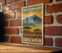 A vintage-style postage stamp depicting Mount Kilimanjaro in Tanzania, with a landscape of trees and a snowy mountain in the background.