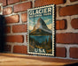 A vintage-style postage stamp featuring a mountain landscape and a lake, mounted on a brick wall.