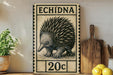 a vintage-style metal stamp with an illustration of an echidna, a type of porcupine, and the text "ECHIDNA 20c" printed on it. The stamp is displayed on a shelf next to a wooden cutting board and some potted plants.