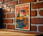 A vintage-style poster of Essaouira, Morocco, featuring a castle, a sailboat, and a bridge, is displayed on a brick wall.
