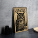 a metal stamp with an illustration of an owl, placed on a table next to some black camera lenses.