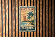 A vintage-style metal sign with the text "MARCO ISLAND FLORIDA USA" is displayed on a wooden wall.