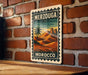 A vintage-style metal sign with the text "MERZOUGA MOROCCO" is displayed on a brick wall, featuring an illustration of a desert landscape with palm trees and mountains.