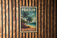 A vintage-style postage stamp featuring a tropical beach scene with palm trees and a rocky shoreline, hanging on a wooden wall.