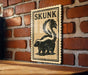 A wooden table with a wooden border, and a framed poster of a skunk on the wall.