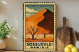 A vintage-style metal sign with a desert landscape and a mountain in the background, featuring the text "SOSSUSVLEI NAMIBIA".