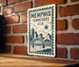 A metal sign with the text "Memphis, Tennessee, USA" and a graphic of a bridge and city skyline is mounted on a brick wall.