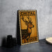 a metal sign with a deer illustration, placed on a table next to some black camera lenses.