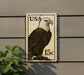 A postage stamp featuring an eagle is displayed on a wall, with a plant visible to the left.