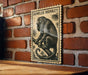 a wooden plaque with a black and white illustration of a monkey sitting on a branch, mounted on a brick wall.