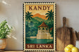 A vintage-style metal sign with a tropical landscape depicting a temple, surrounded by palm trees and mountains, with the text "KANDY" and "SRI LANKA" printed on it. The sign is displayed on a shelf next to a wooden cutting board and a potted plant.