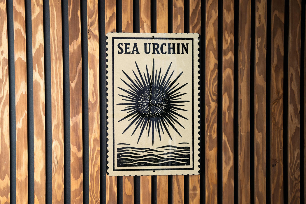 a sign with the text "SEA URCIN" and a sunburst design, mounted on a wooden wall.