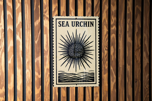 a sign with the text "SEA URCIN" and a sunburst design, mounted on a wooden wall.