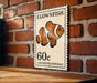 A clownfish postage stamp is displayed on a brick wall, featuring an illustration of the clownfish and the denomination of 60 cents.