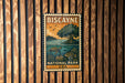 A vintage-style metal sign for Biscayne National Park in the United States, featuring an illustration of a turtle and a tree.