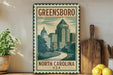 A vintage-style metal sign with a cityscape illustration and the text "GREENSBORO NORTH CAROLINA USA" is displayed on a shelf, accompanied by a wooden cutting board and a potted plant.