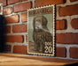 A vintage-style postage stamp featuring a large, shaggy dog with the text "BERGAMASCO" and "DOG 20" printed on it, mounted on a brick wall.