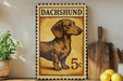A vintage-style metal stamp featuring a dachshund dog, with the text "DACHSHUND" and the denomination "5c" printed on it. The stamp is displayed on a shelf next to a wooden cutting board and a potted plant.
