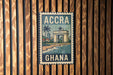 A vintage-style metal sign with the text "ACCRA GHANA" displayed prominently, featuring an illustration of a building and palm trees.
