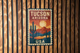 A vintage-style postage stamp from Tucson, Arizona, featuring a desert landscape with cacti and mountains in the background.