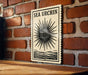 a wooden table with a framed poster or sign hanging on the wall behind it. The poster has a black and white design with a sunburst pattern and the text "SEA URCIN" written on it.