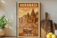 A vintage-style poster of Varanasi, India, featuring a boat on the water and a temple in the background. The poster is framed and displayed on a shelf, with a potted plant and a cutting board nearby.