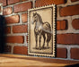 a wooden table with a framed illustration of a horse on it, mounted on a brick wall.