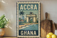 a vintage-style metal sign with the text "ACCRA GHANA" and an illustration of a building, palm tree, and beach. The sign is displayed on a shelf next to a wooden cutting board and a potted plant.