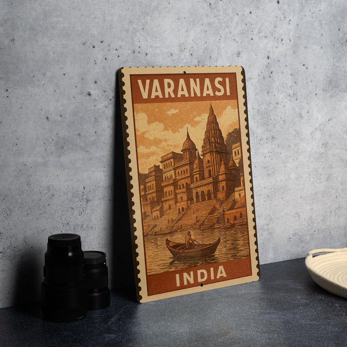 A vintage-style metal sign with the text "VARANASI INDIA" and an illustration of a temple or palace, along with a boat in the water, is displayed on a gray concrete surface.