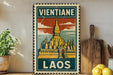 A vintage-style metal sign with a temple illustration and the text "Vientiane Laos" is displayed on a shelf, accompanied by a potted plant, a wooden cutting board, and some lemons.
