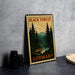 A vintage-style metal stamp depicting a forest scene with pine trees and a river, placed on a gray countertop next to some black camera lenses.