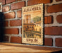 A vintage-style poster of Alhambra, Spain, displayed on a brick wall.