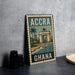 A metal sign with the text "ACCRA GHANA" and an illustration of a cityscape with a palm tree, placed on a gray countertop next to some black camera lenses.
