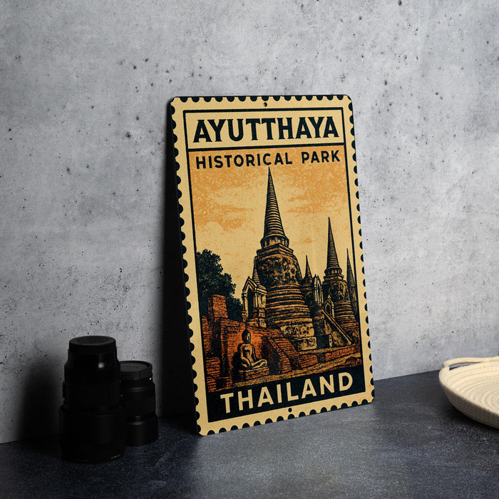 A metal sign with the text "AYUTHAYA HISTORICAL PARK THAILAND" and an illustration of a temple, placed on a table next to some black camera lenses.